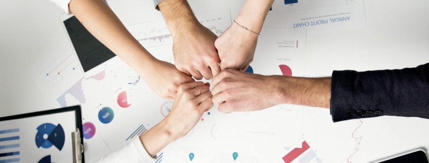 Free Colleagues celebrate success with a fist bump over financial charts depicting teamwork and unity. Stock Photo