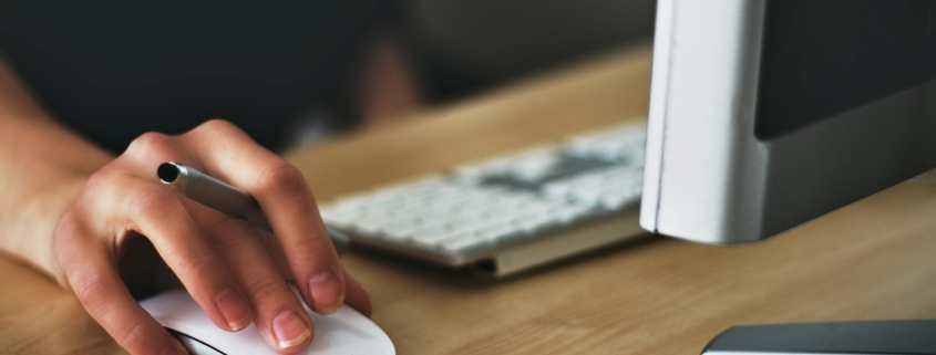 Free A hand using a wireless mouse at a modern desk setup with a computer and keyboard. Stock Photo
