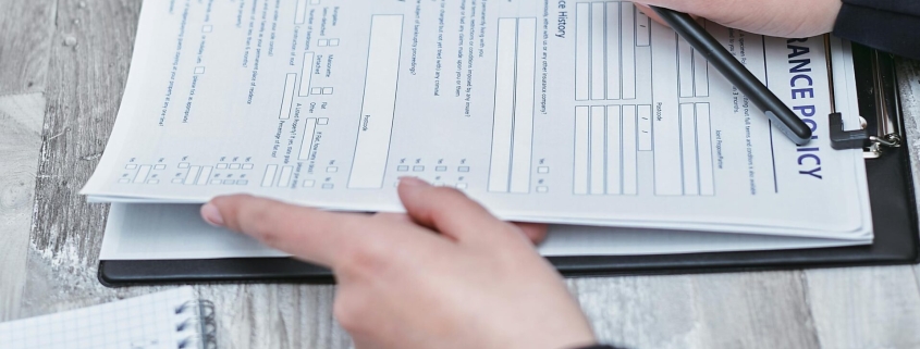 Free Close-up of hands analyzing insurance policy paperwork with pen on table. Stock Photo
